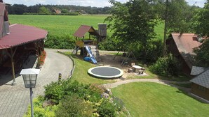 A playground with a slide, a swing set, and a trampoline surrounded by a well-maintained lawn and garden. - Ferienanlage Karolinenhof 2 (Haundorf)