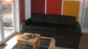 A living room with a black sofa, a wooden coffee table, and a red and yellow wall. - Ferienanlage Karolinenhof 2 (Haundorf)