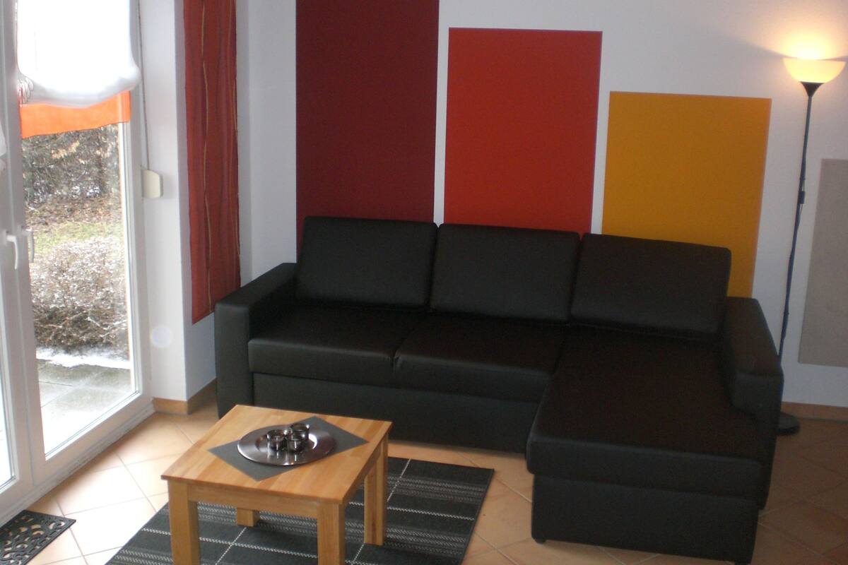 A living room with a black sofa, a wooden coffee table, and a red and yellow wall.