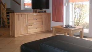 A living room with a sofa, wooden cabinet, television, and a window with curtains. - Ferienanlage Karolinenhof 2 (Haundorf)