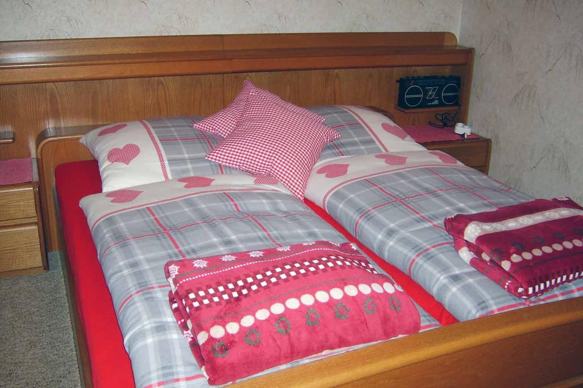 A bed with a plaid bedspread, multiple pillows, and a red blanket.