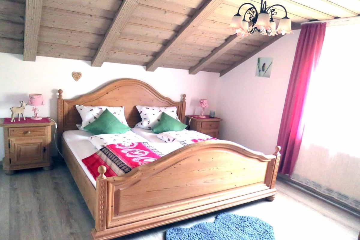 A wooden bed with a headboard, two bedside tables, a blue rug, and a chandelier.