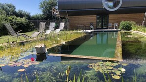 Um edifício moderno com uma piscina grande, rodeado por espreguiçadeiras e um deck de madeira.