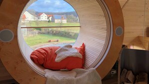 Cômodo circular com janela que oferece vista para casas e paisagem verde.