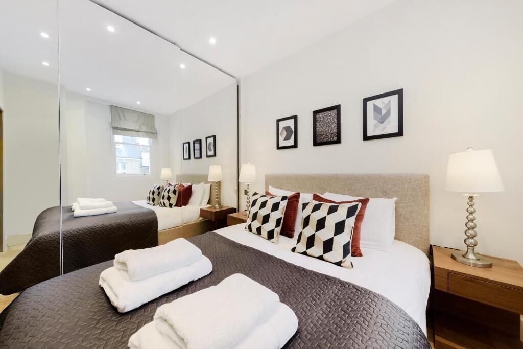 Une chambre d’hôtel avec un grand lit, un lit plus petit, un miroir, des lampes de chevet et des tableaux encadrés au mur.