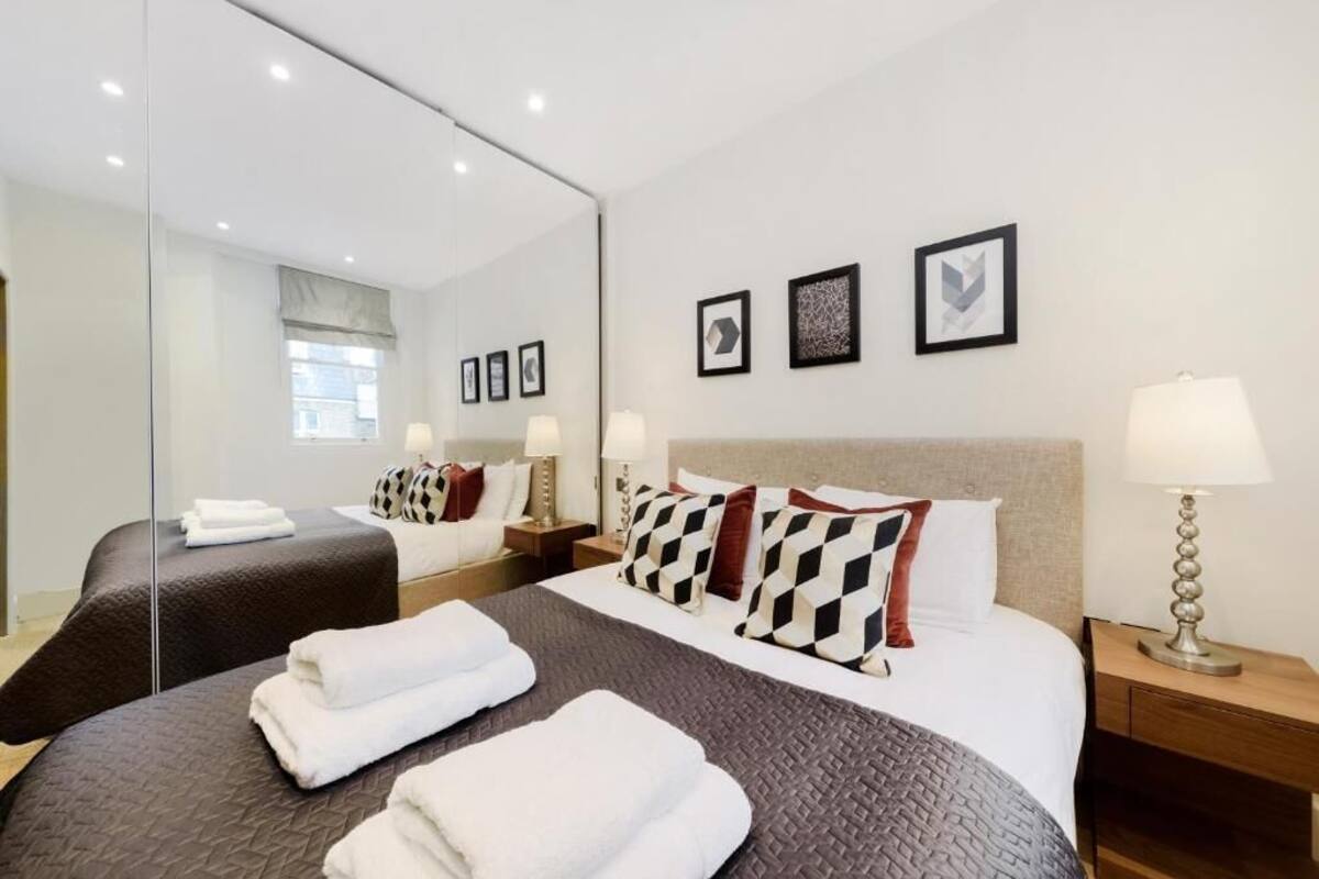 Une chambre d’hôtel avec un grand lit, un lit plus petit, un miroir, des lampes de chevet et des tableaux encadrés au mur.