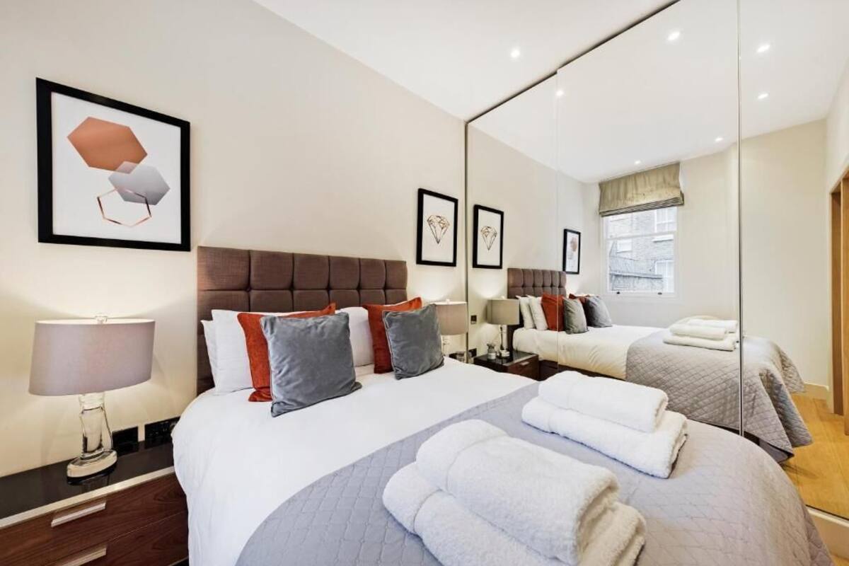 Une chambre d’hôtel avec un grand lit, une table de chevet avec une lampe, un miroir et des œuvres d’art accrochées au mur.