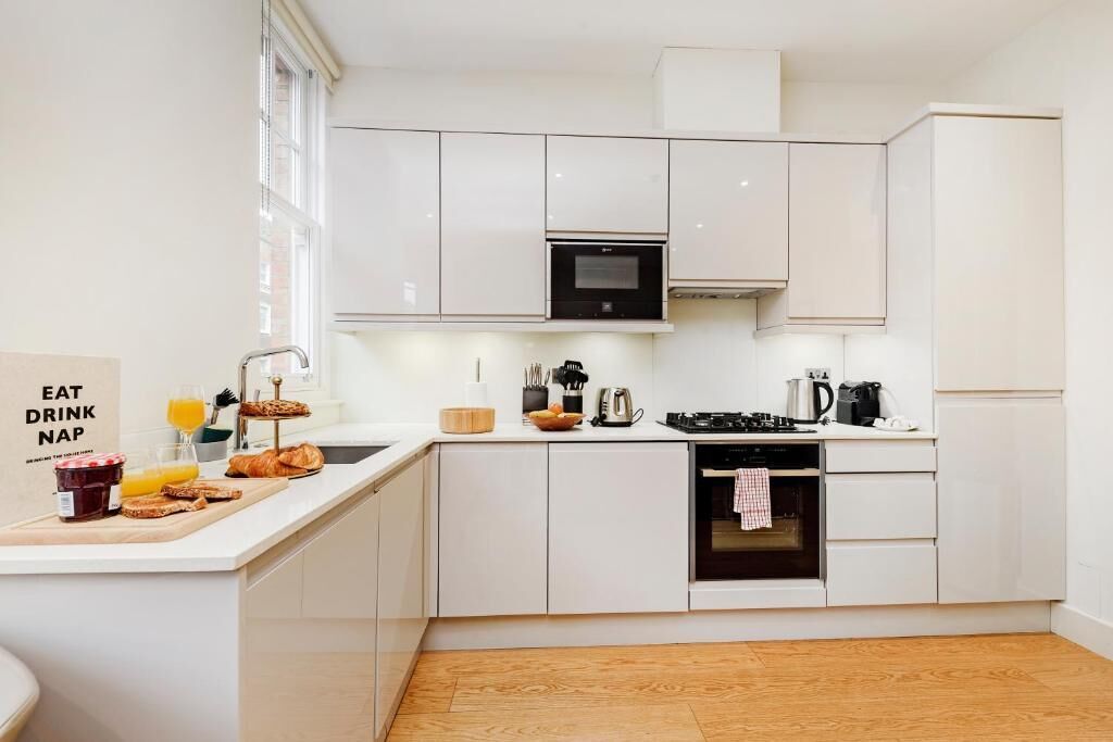 Une cuisine moderne avec des meubles blancs, un four encastré et un bar pour prendre le petit-déjeuner, où l’on peut déguster des plats et des boissons.