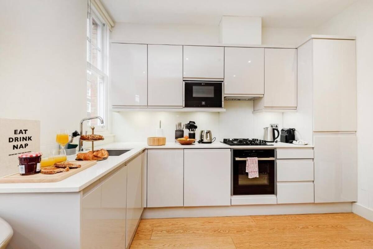 Une cuisine moderne avec des meubles blancs, un four encastré et un bar pour prendre le petit-déjeuner, où l’on peut déguster des plats et des boissons.