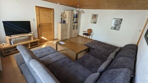 Un salon moderne avec un grand canapé d’angle gris, un meuble TV en bois et un plafond en bois.