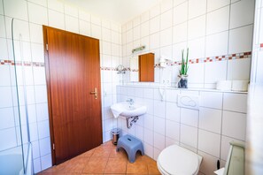 Bathroom features a sink, toilet, and step stool, with a shelf for toiletries and a plant.