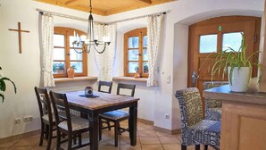 A dining area with a wooden table and chairs, a chandelier, and windows with curtains.
