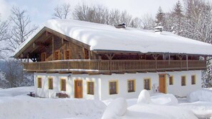 A chalet-style building with a wooden balcony and multiple windows, surrounded by snow.