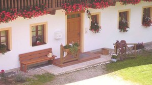 A white building with a wooden balcony, a wooden bench, and a horse statue.