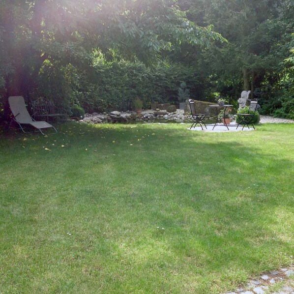 A grassy backyard with a patio table and chairs, surrounded by dense foliage and a stone wall. - Ferienwohnung Buchbergblick (Coburg)