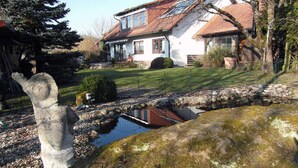 Une maison avec un chemin de pierre menant à un étang, le tout entouré d’une pelouse bien entretenue et d’arbres.