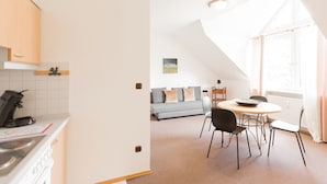 A modern kitchen with white cabinets and a coffee machine, a dining area with a round table and chairs, and a living room with a sofa and a painting on the wall. - Pension Lutter (Bodenwoehr)