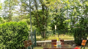 An outdoor seating area with a table and chairs, surrounded by greenery and trees. - Pension Lutter (Bodenwoehr)