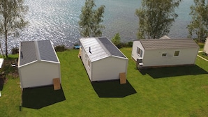 A row of mobile homes with a lake view, each with a distinct roof style and positioned on a grassy area. - Pension Lutter (Bodenwoehr)