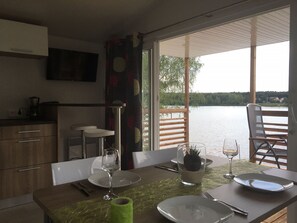 A dining area with a table set for two, a view of a lake, and a kitchen area with a coffee maker. - Pension Lutter (Bodenwoehr)