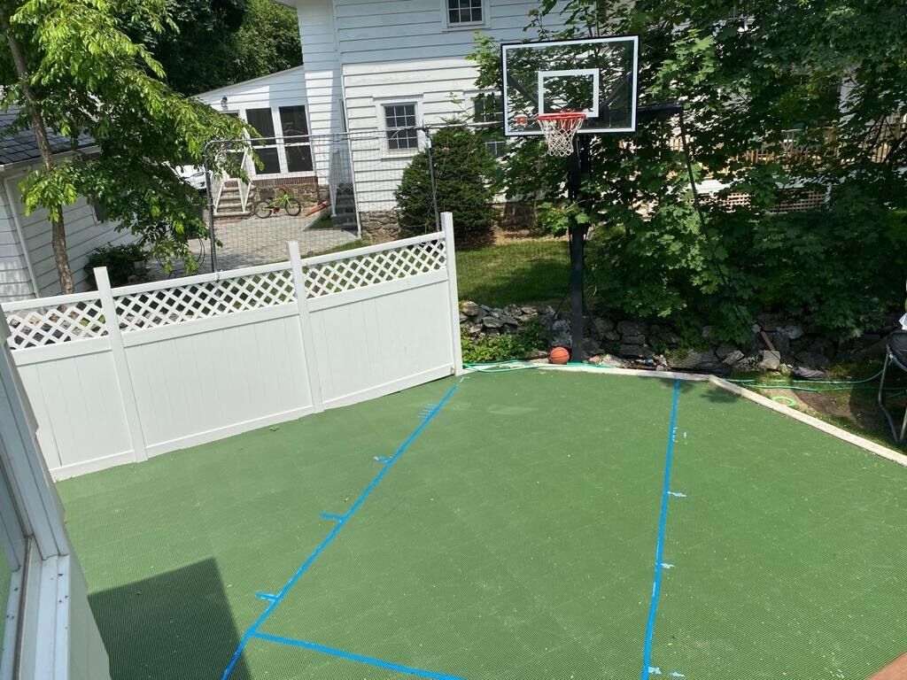 An outdoor basketball court with a white fence and trees in the background.