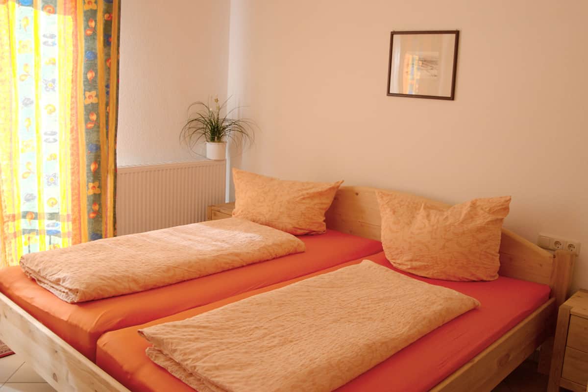 Un lit double avec une literie orange, une plante en pot et un tableau encadré accroché au mur.