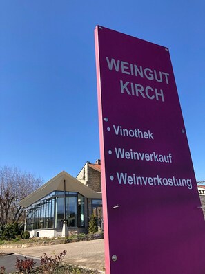 Une enseigne pour le domaine viticole Weingut Kirch, avec une liste à puces indiquant : Vinothèque, vente de vin et dégustation de vin.