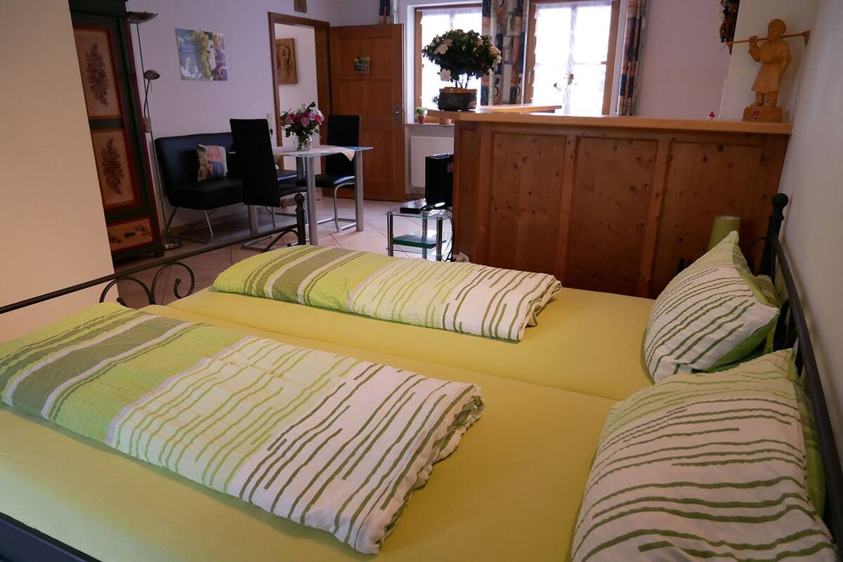 Un lit double avec une literie à rayures, une tête de lit en bois et une petite table avec des chaises à l’arrière-plan.