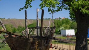 Une structure en bois représentant un navire de pirate, avec un drapeau, située dans un parc. On aperçoit un arbre et une clôture en arrière-plan.