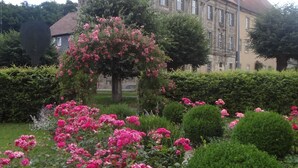 Un edificio de techo rojo y arquitectura clásica, rodeado de jardines bien cuidados con rosas rosadas.