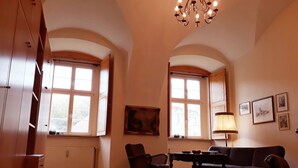Amplia sala de estar con techos altos, ventanas grandes, candelabro, sofá, mesa de comedor y una silla.
