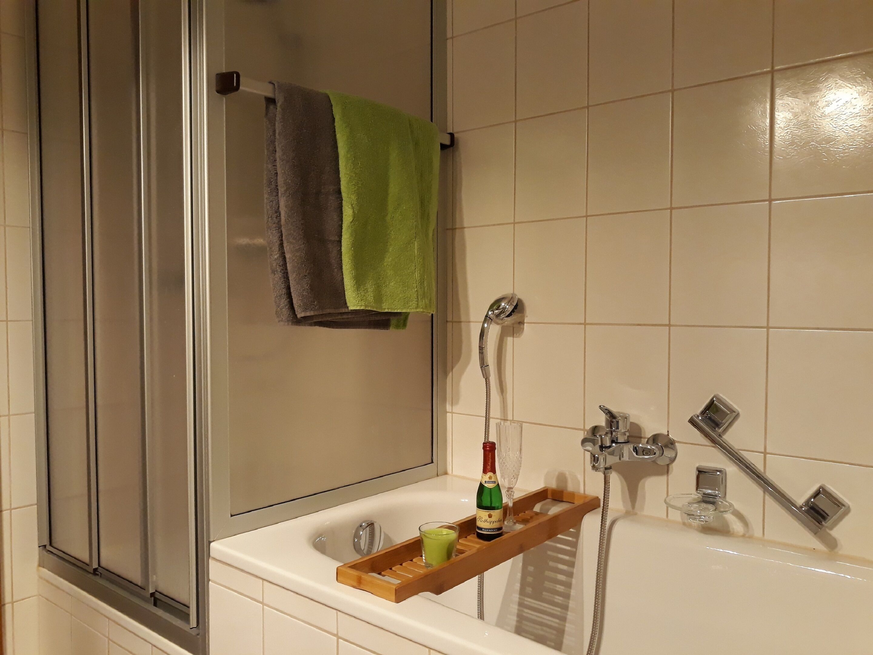 A bathroom with a bathtub, a glass-enclosed shower, and a towel rack with a green towel.