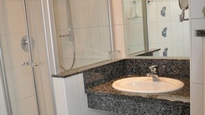 Un baño con ducha compartimentada con vidrio, lavamanos de encimera de granito, espejo y toallero.