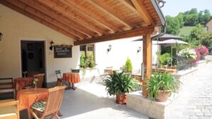 Un patio al aire libre con mesas y sillas de madera, plantas en macetas y un letrero que indica un restaurante.