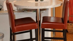 Una pequeña mesa redonda con dos sillas de cuero marrón, un jarrón con una flor roja y una figurita sobre la mesa.