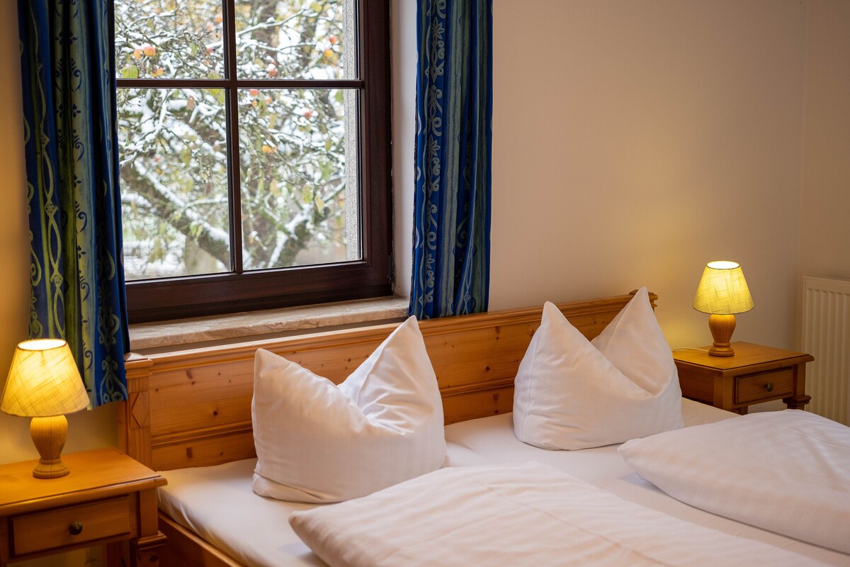 Un dormitorio con cabecera de madera, dos mesitas de noche con lámparas y una ventana con cortinas.