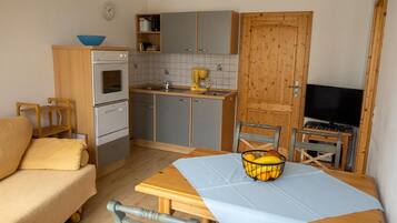 A compact kitchen with a dining table, a sofa, and a television.