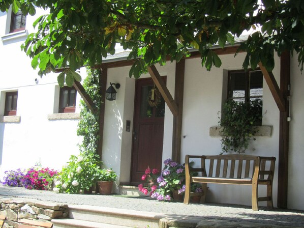 A traditional building with a wooden bench outside, a stone wall, and potted plants. - Bio Ferienhof Erzengel (Berg)