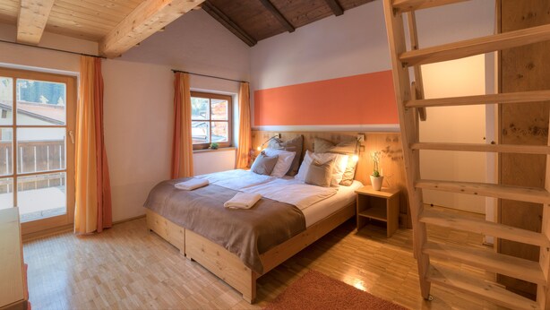 A bedroom with a wooden bed, a nightstand, a window with curtains, and a wooden ladder. - Chalet Murr by Skinetworks (Sankt Anton am Arlberg)