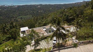 A modern building with a flat roof, surrounded by lush greenery and a view of the ocean. - Villa Zest at Lime Samui (Koh Samui)