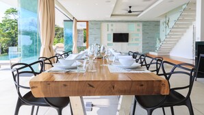 A dining area with a wooden table set for six, surrounded by black chairs, with a glass partition and a view of greenery outside. - Villa Zest at Lime Samui (Koh Samui)