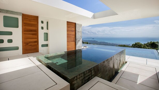 A modern infinity pool with a clear view of the ocean and a cityscape in the background. - Villa Zest at Lime Samui (Koh Samui)