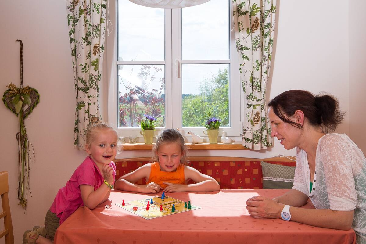 A room with a large window, a table with a red tablecloth, and a plant on the windowsill.
