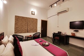 A hotel room with a bed, desk, chair, television, and an air conditioning unit. - Dera Kumbhalgarh (Kumbhalgarh)
