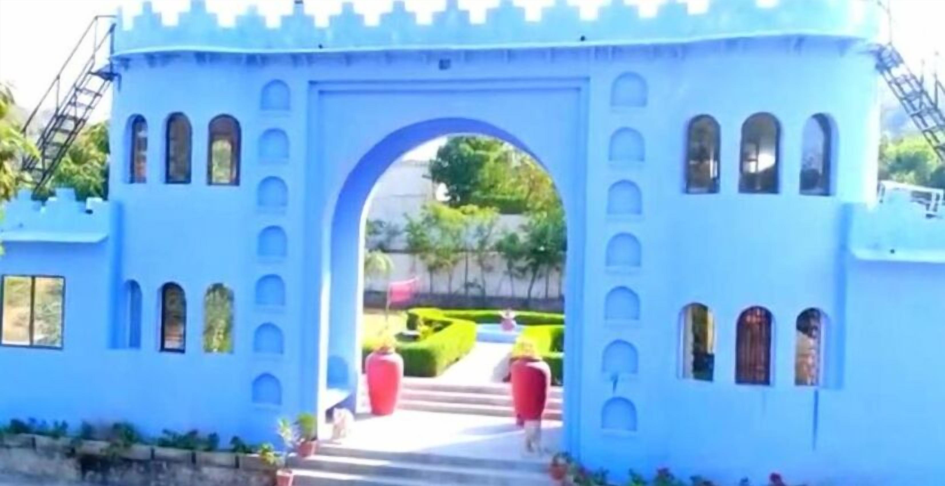Eine blaue, schlösserähnliche Struktur mit Rundbogenfenstern und einem zentralen Bogen.