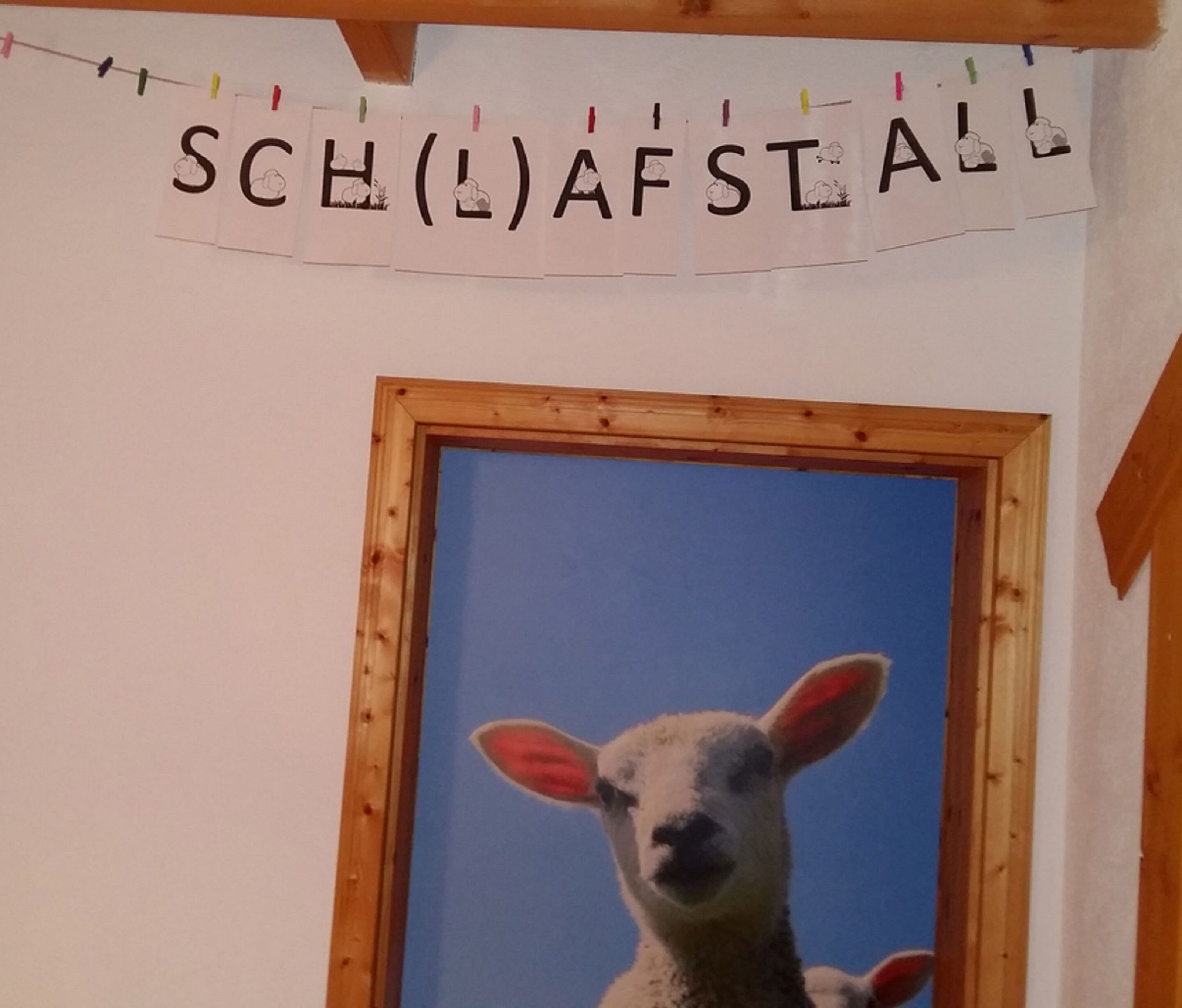 A room with a framed picture of a sheep, a banner with letters, and a wooden beam structure.