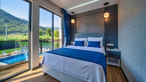 Une chambre moderne avec un grand lit, une vue sur une piscine et sur la verdure, ainsi qu’une table de chevet avec un téléphone.