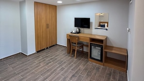 Une chambre avec un bureau en bois, une télévision, un petit réfrigérateur et une armoire.