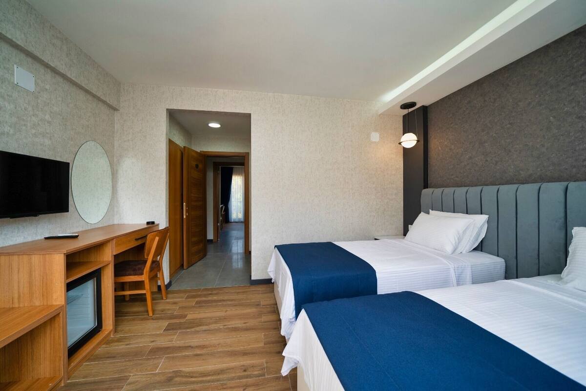 Een hotelkamer met twee bedden, een bureau met een stoel, een televisie en een gang naar een andere kamer.