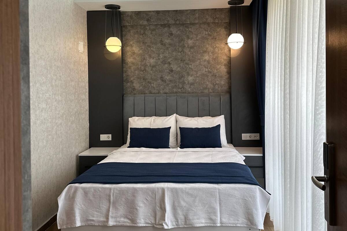 Een moderne hotelkamer met een groot bed, een donker hoofdeinde en twee bedlampjes.